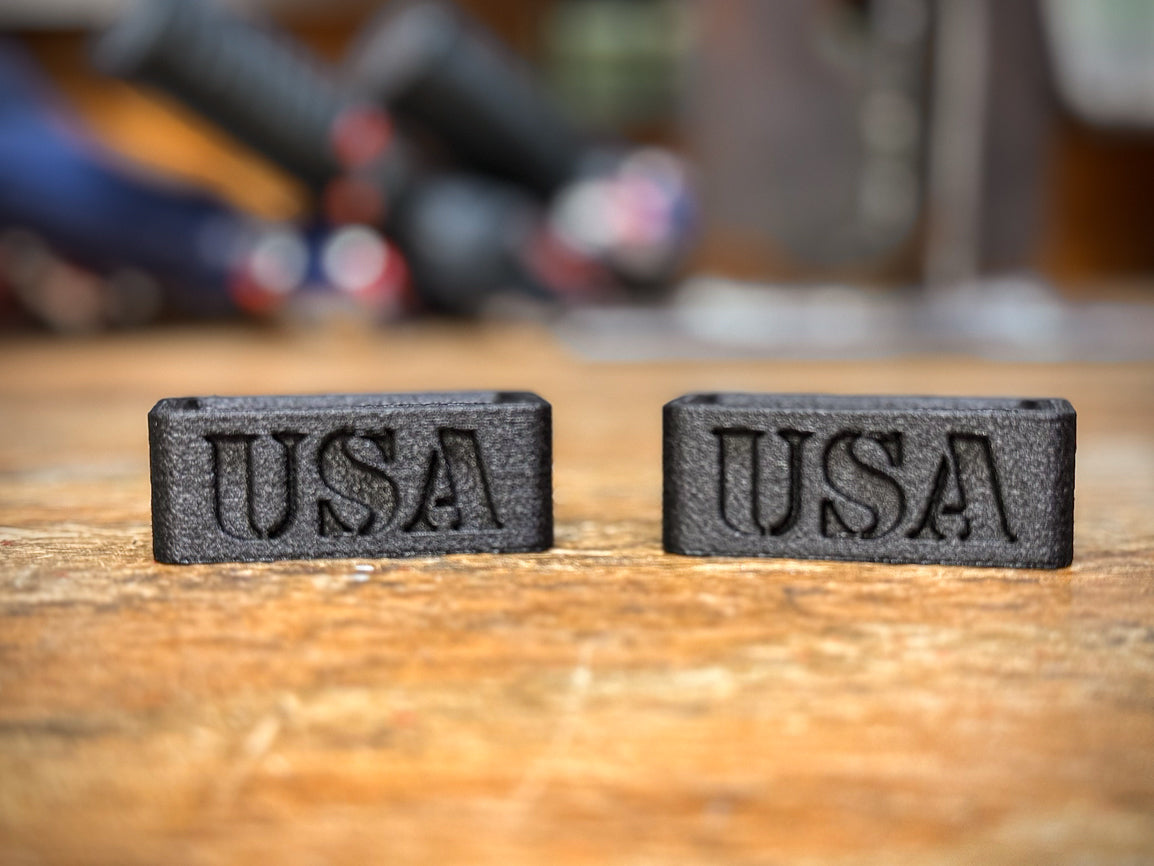 Two black belt clips with the text 'USA' embossed on them, placed on a wooden surface.